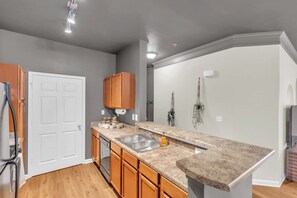 A kitchen with wooden cabinets, a granite countertop, a double sink, and a white door. - Pool, Gym & Central Location! 2- King Beds (Spartanburg)