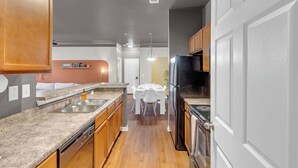 Eine moderne Küche mit Holzschränken, einer Granit Arbeitsplatte, einem schwarzen Kühlschrank und einem Essbereich mit weißen Stühlen und einem Tisch.