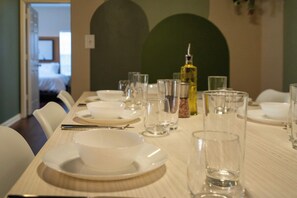 Mesa de jantar posta com pratos, tigelas e copos, com uma garrafa de azeite sobre a mesa.
