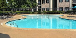 A swimming pool with a pool ladder, surrounded by lounge chairs and a brick building in the background.