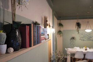 A room with a bookshelf, a dining table, and hanging plants. - 3 King Beds, Perfect for Long Stays (Spartanburg)