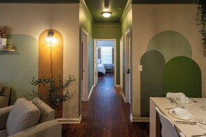 A hallway with a dining area on the right, a sofa on the left, and a bed at the end.