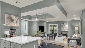A modern kitchen with a large island, a dining area with a table and chairs, and a living room with a sofa and a TV.