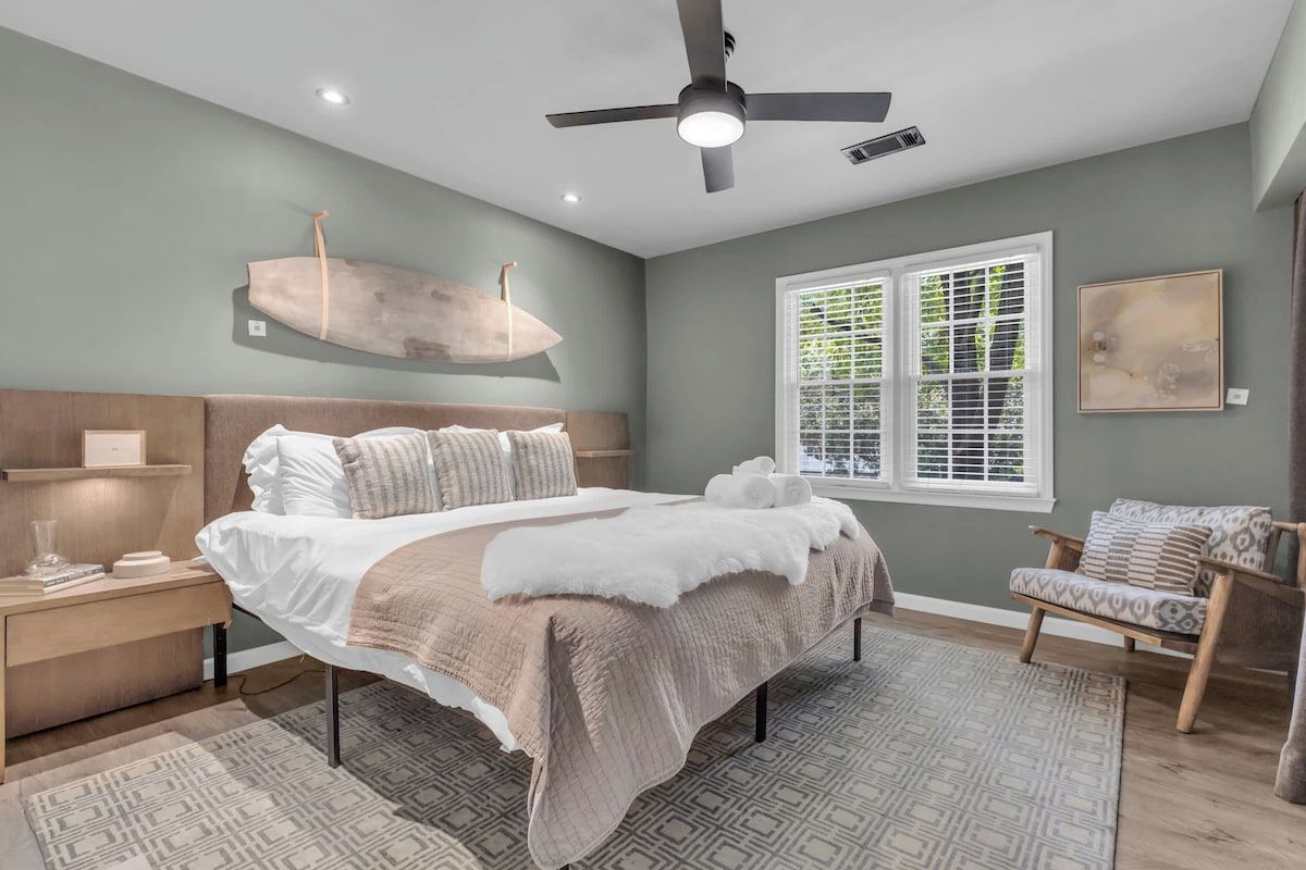 A bedroom with a bed, nightstands, a ceiling fan, a window with blinds, and a chair.