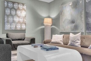 Ein modernes Wohnzimmer mit einem weißen Sofa, einem grauen Sessel und einem Couchtisch mit Büchern.