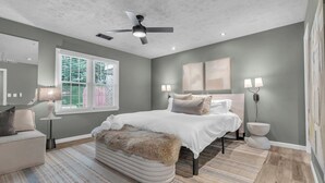 Ein Schlafzimmer mit Bett, Deckenventilator, Fenster und Bildern an der Wand.