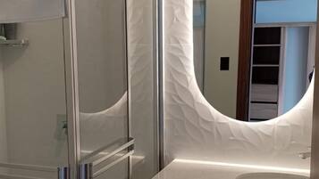 Une salle de bain moderne avec une douche à parois de verre, un mur blanc à texture et un meuble-lavabo en bois avec un miroir.