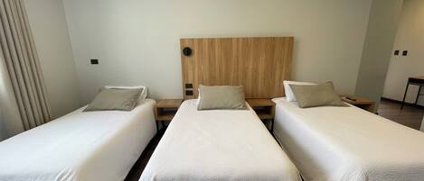 Une chambre d’hôtel avec trois lits simples, chacun doté d’une tête de lit en bois et d’une petite table de chevet en bois.
