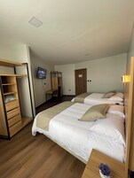Un dormitorio con dos camas, un armario de madera, un televisor en la pared y una mesita con un florero.