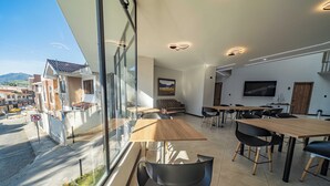 A modern dining area with large windows, wooden tables, and black chairs.