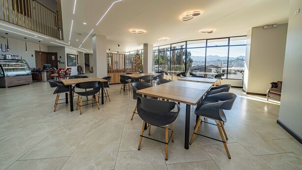A modern dining area with multiple tables and chairs, a counter with a display case, and large windows offering a view.