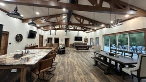 A spacious room with a high ceiling, wooden beams, a pool table, and a large window offering a view of the outdoors. - Rippling Waters! 3 BD 2.5 BA Riverfront Home, 8 min. from airport.  Sleeps 11. (Mills River)