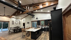 A spacious kitchen with a large island, wooden beams, and a dining area with a view to the outside. - Rippling Waters! 3 BD 2.5 BA Riverfront Home, 8 min. from airport.  Sleeps 11. (Mills River)
