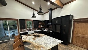 A modern kitchen with a large island, dark cabinetry, and a view to the outdoors. - Rippling Waters! 3 BD 2.5 BA Riverfront Home, 8 min. from airport.  Sleeps 11. (Mills River)
