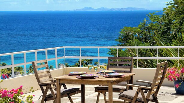 A wooden table with chairs on a balcony overlooking the ocean.