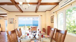 A dining area with a glass table, wicker chairs, and a view of the ocean.