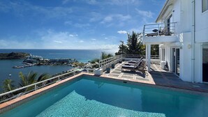 A swimming pool with a view of the sea and a white building with a balcony.