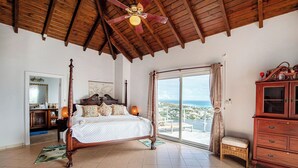A spacious bedroom with a four-poster bed, a wooden ceiling, and a view of the ocean.