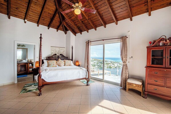 Un dormitorio espacioso con cama con dosel, techo de madera y vista al océano.