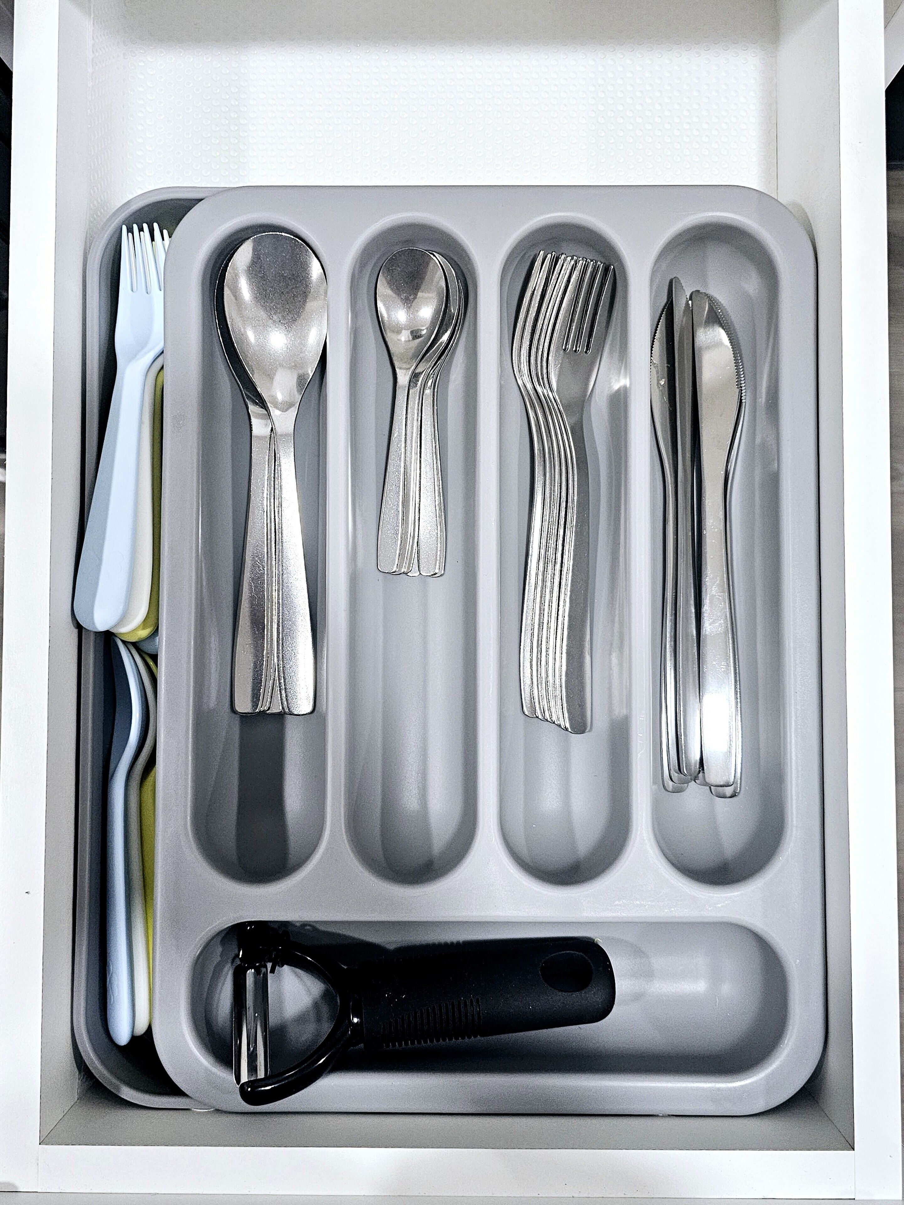 A drawer containing a set of silverware including a fork, spoon, knife, and a grater.