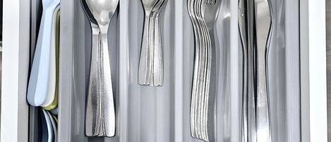 A drawer containing a set of silverware including a fork, spoon, knife, and a grater.