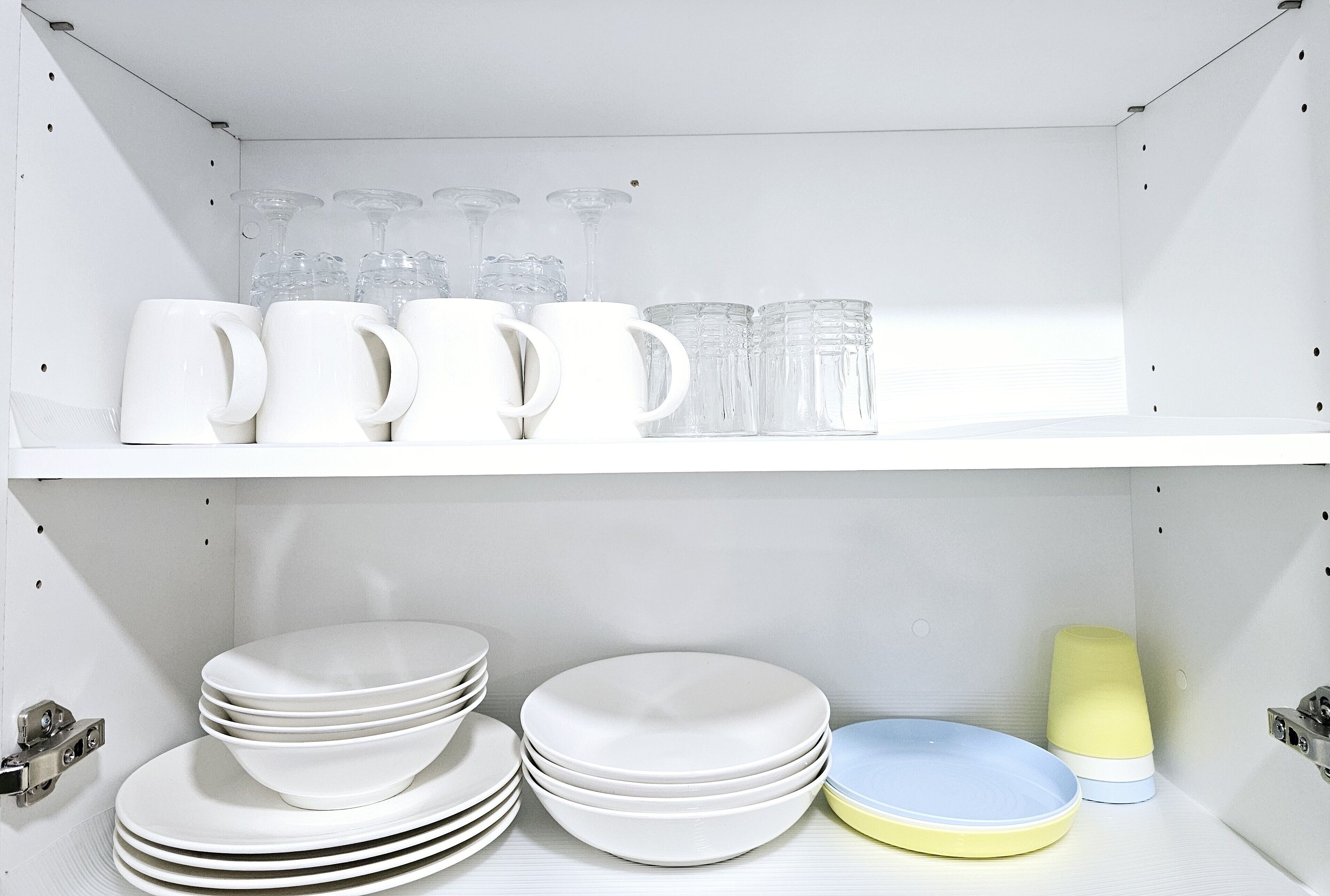 Un módulo de almacenamiento blanco con estantes que contienen tazas blancas, vasos de vidrio y platos.