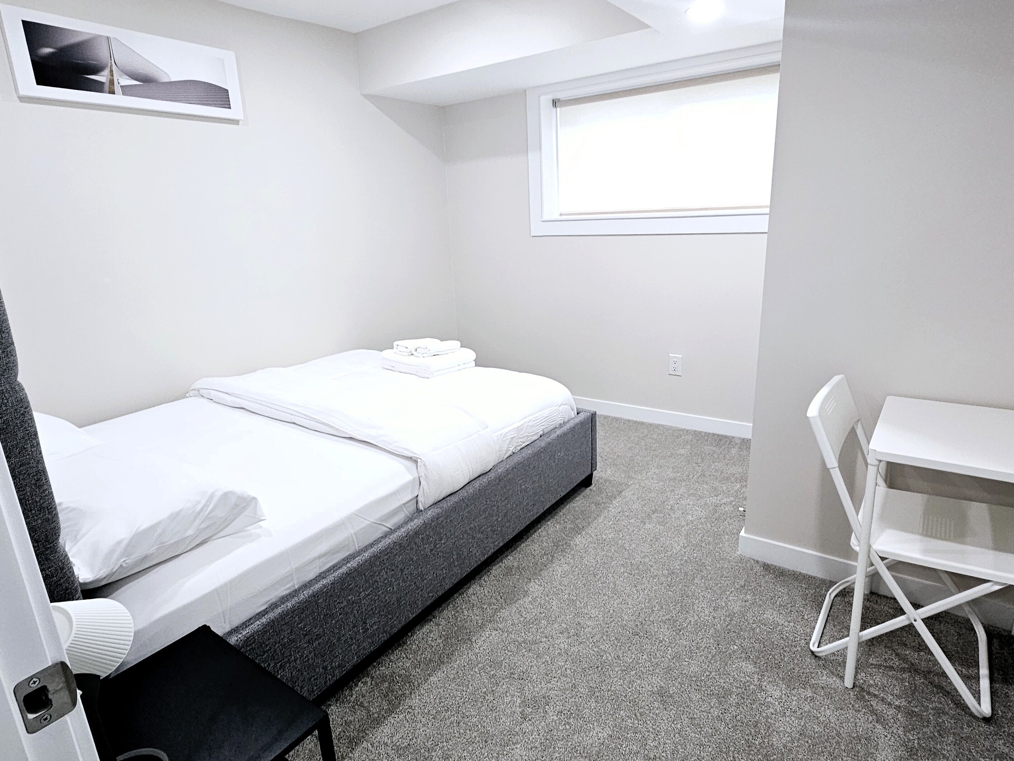 A small, neatly arranged bedroom with a bed, a desk, and a chair.