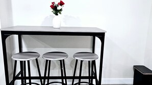 Een kleine, moderne keuken met een wit aanrecht, drie krukken en een vaas met bloemen.