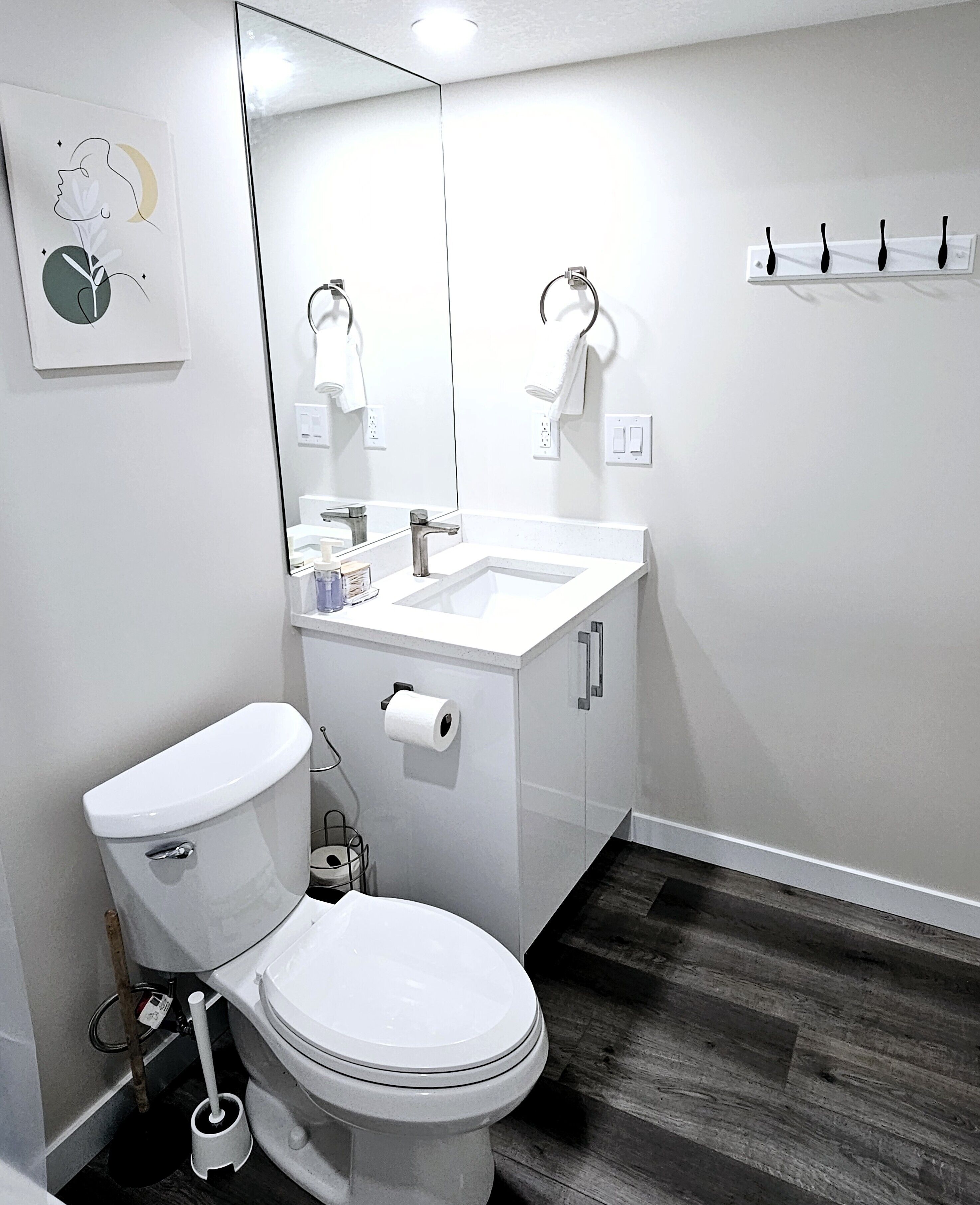 A modern bathroom with a white toilet, a sink with a mirror above it, and a wooden floor.