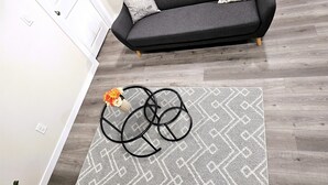 Een moderne woonkamer met een donkergrijze bank, een kamerbreed tapijt met een patroon en een vaas met bloemen.
