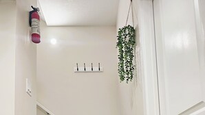 Een trap met houten treden, witte muren, een brandblusser, een hangplant en een deur.