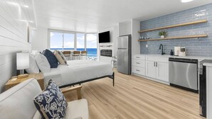 A modern bedroom with a bed, bedside table, and a view of the ocean. The room has a wooden floor and white walls. - Beach Front Ocean View Condo - Top of the Gulf 521 (Panama City Beach)