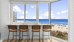 A room with a large bay window overlooking a beach. There are four wooden chairs aligned in front of the window. - Beach Front Ocean View Condo - Top of the Gulf 521 (Panama City Beach)