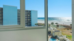 A view from a window overlooking a beach with a pool area and a building in the background.