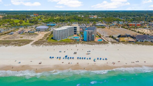 An aerial view of a coastal hotel with multiple buildings, a sandy beach, and a clear blue sky.