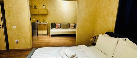 A hotel room with a bed, a small kitchenette, a sofa, and an air conditioning unit.