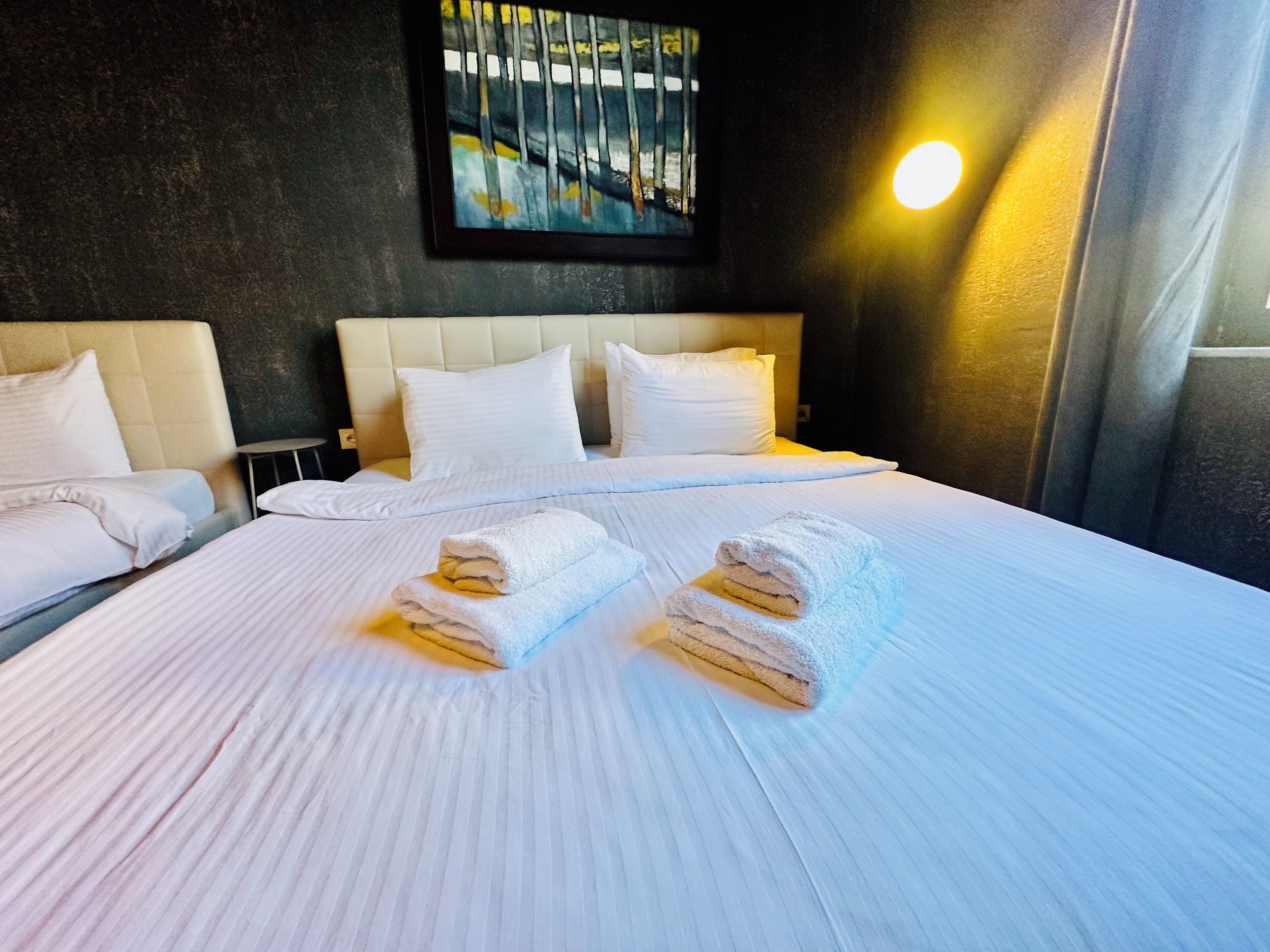 A hotel room with a large bed, two pillows, a headboard, a painting on the wall, and a bedside lamp.