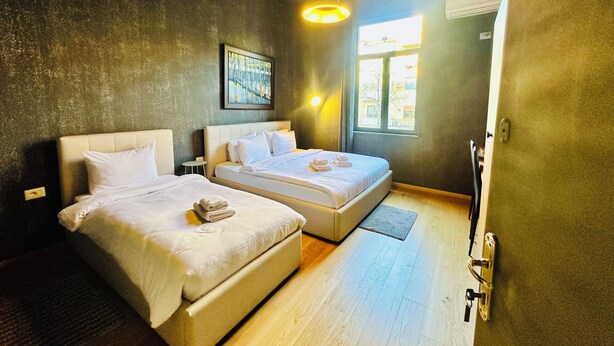 A bedroom with two beds, a window, and a hanging light fixture. - SA Studio 24 (Tirana)