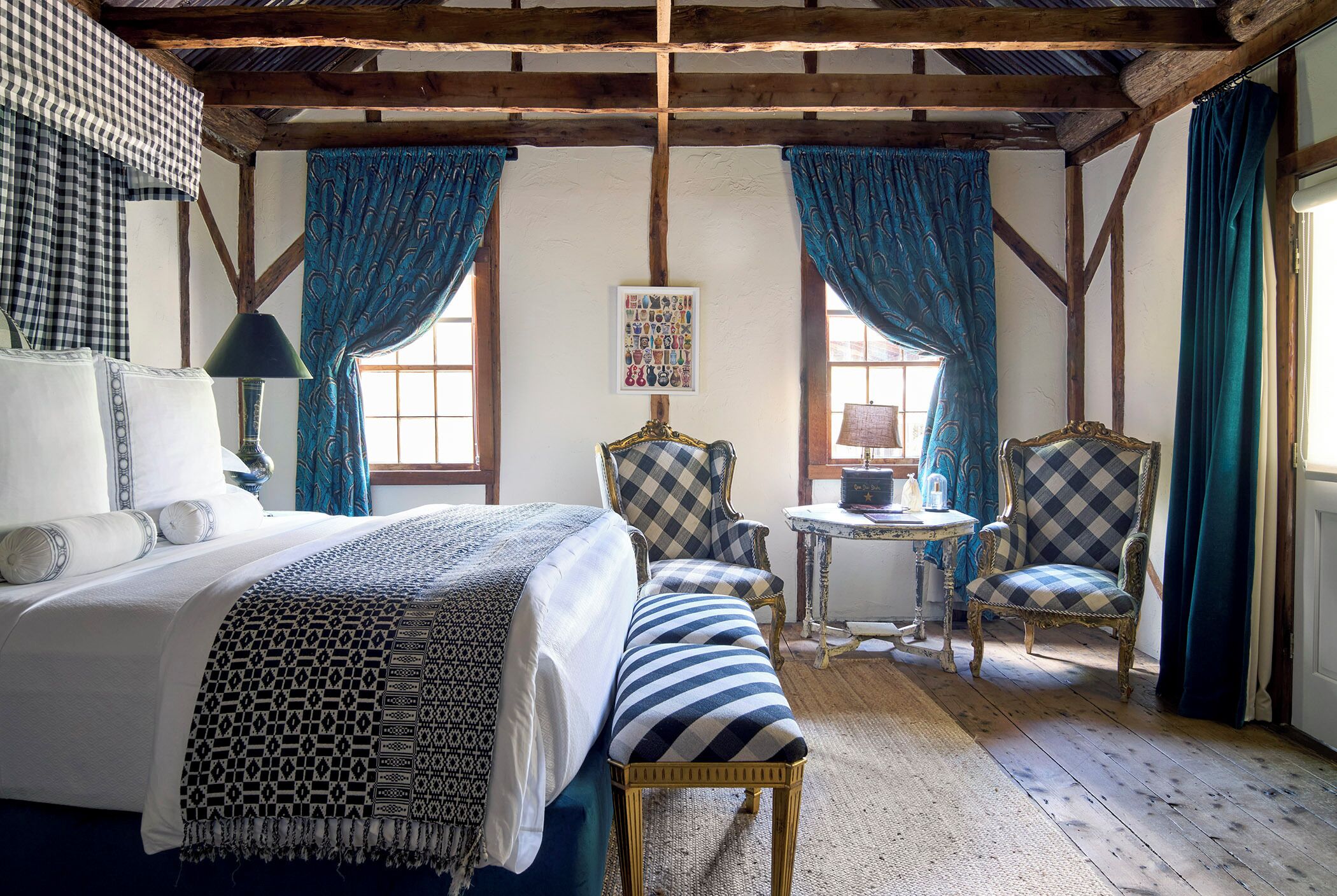 A bedroom with a bed, two chairs, a small table, and a window with curtains.