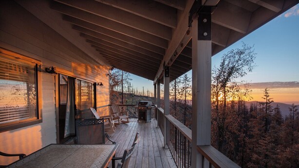 A wooden deck with outdoor seating and a grill, overlooking a forested landscape. - Charming and Relaxing Getaway with Great Views (Shaver Lake)