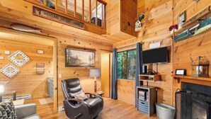 A cabin interior with a fireplace, a mounted television, a leather recliner, and a painting on the wall.