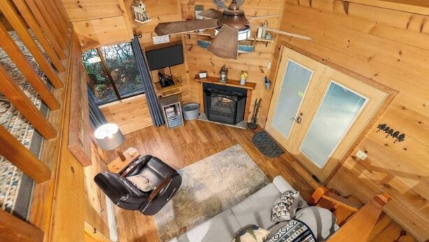 A cozy cabin interior with a fireplace, a sofa, a dining table, and a ceiling fan.
