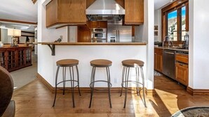 A modern kitchen with wooden cabinets, stainless steel appliances, and three bar stools. - Ski in, Ski out 3 Bedroom Condo at the Beaver Creek Lodge (Avon)