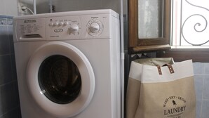 A front-loading washing machine with a control panel and a shopping bag labeled "WASH DRY IRON LAUNDRY DELUXE" next to it.