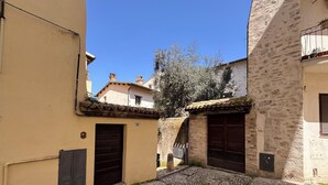 A narrow cobblestone street with buildings on either side, featuring traditional stone facades and dark wooden doors.