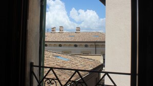 A view from a balcony with a tiled roof and chimneys, overlooking a building with a white facade and arched windows.