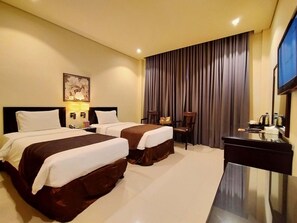 Quarto de hotel com duas camas, uma mesa de trabalho, televisão e uma janela grande com cortinas.