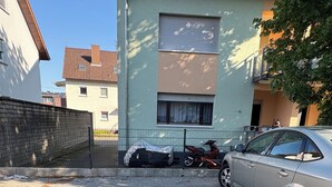 Un área de estacionamiento con un coche y una motocicleta, un edificio con techo de tejas y una valla.