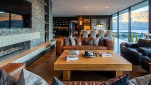 A spacious living area with a stone fireplace, leather sofas, and a large wooden coffee table. - The Belfast (Queenstown)