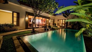 A modern pool area with a clear view of the pool, a lounge chair, and a well-lit interior space with large windows.